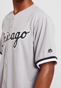 Jersey de béisbol gris con el logotipo de "Chicago" en blanco y negro. Presenta un frontal de botones, cuello de canalé y mangas en contraste en blanco y negro.