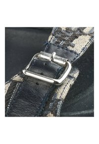 Gros plan d'une boucle métallique argentée fixant une sangle en tissu bleu à motif avec des détails en cuir.