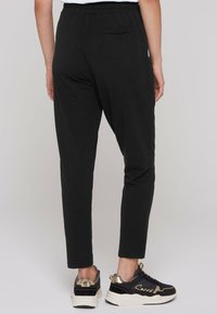 Zwarte tapse broeken van zachte stof, met een elastische tailleband en een enkele achterzak. Gepaard met zwarte en gouden sneakers.