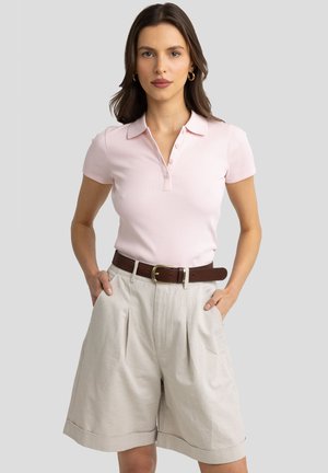 Polo shirt a righe di un rosa chiaro con colletto e tre bottoni, abbinato a pantaloni corti beige plissettati e una cintura di pelle marrone.