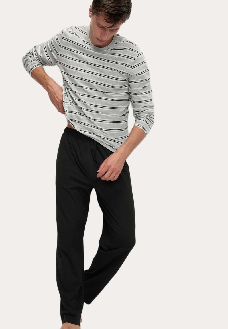 Camicia a maniche lunghe grigia a righe con accenti neri, abbinata a pantaloni neri con coulisse. Tessuto morbido, vestibilità rilassata, design casual.