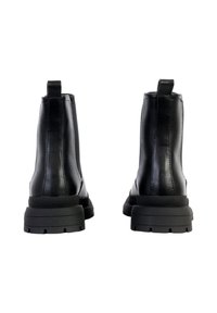 Botas de tobillo de cuero negro con un acabado suave, suela de goma gruesa y tirador en la parte trasera para facilitar su uso. Diseño minimalista, sin acentos.