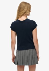 Marineblauw top met korte mouwen en een ronde hals, verfraaid met stiksels, gecombineerd met een grijs gestreepte geplooide rok voor een gecoördineerde uitstraling.