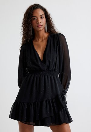 Schwarz kleid mit langen ärmeln und einem tiefen V-Ausschnitt. Verfügt über eine geraffte taille und einen mehrstufigen Rüschensaum. Durchsichtiges material mit kleinen metallischen akzenten.