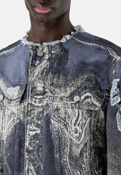 Gros plan d'une personne portant une veste en denim délavée avec un col effiloché et un motif abstrait noir et blanc tourbillonnant, boutonnée à l'avant.