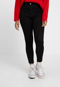 Jeans negros de cintura alta con un ajuste slim, ligero elasticidad, cierre frontal con botón y diseño de cinco bolsillos, combinados con zapatillas blancas.