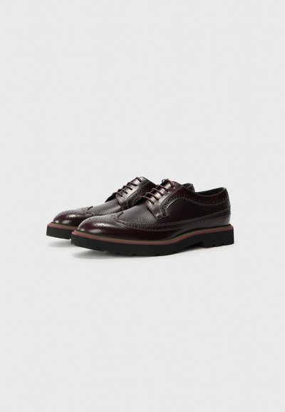 Scarpe in pelle bordeaux scuro con dettagli perforati, punta rotonda e suola in gomma nera a contrasto. I lacci passano attraverso sei occhielli.