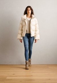 Μπεζ φούτερ μπουφάν με υψηλό γιακά, συνδυασμένο με ένα ανοιχτό πουλόβερ, μπλε τζιν και καφέ μποτάκια μέχρι τον αστράγαλο. Λείος υφή και ραφή χαλιού.