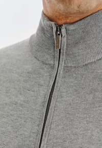 Szary sweter na zamek błyskawiczny z wysokim kołnierzem, wykonany z miękkiej dzianiny. Posiada metalowy zamek i subtelny wzór tekstury.