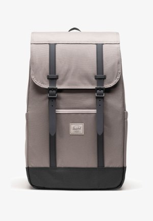 Sivá látková batoh s čiernymi popruhmi, sponami a dnom, ktorý má predné vrecko a malú obdĺžnikovú značkovú nášivku.