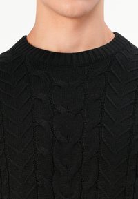 Maglione nero lavorato a maglia con scollo rotondo e motivo a treccia. La texture è spessa e a coste, con dettagli intrecciati in rilievo.