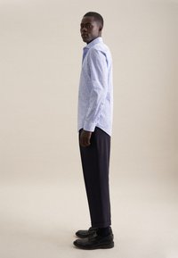 Lichtblauw langemouwen shirt met een subtiel patroon, gecombineerd met donkere broeken en zwarte schoenen. Glad fabric met een getailleerde pasvorm.