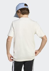 T-shirt crème à manches courtes avec une coupe décontractée, texture lisse et encolure arrondie, associé à un pantalon noir avec des rayures blanches.