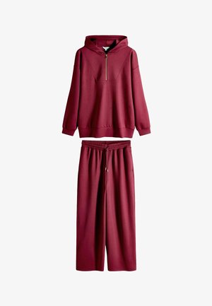 Bordeauxroter Kapuzenpullover mit halbem Reißverschluss, kombiniert mit passenden Sweatpants mit weitem Bein. Hergestellt aus weichem, strukturiertem Stoff mit elastischem Bund.