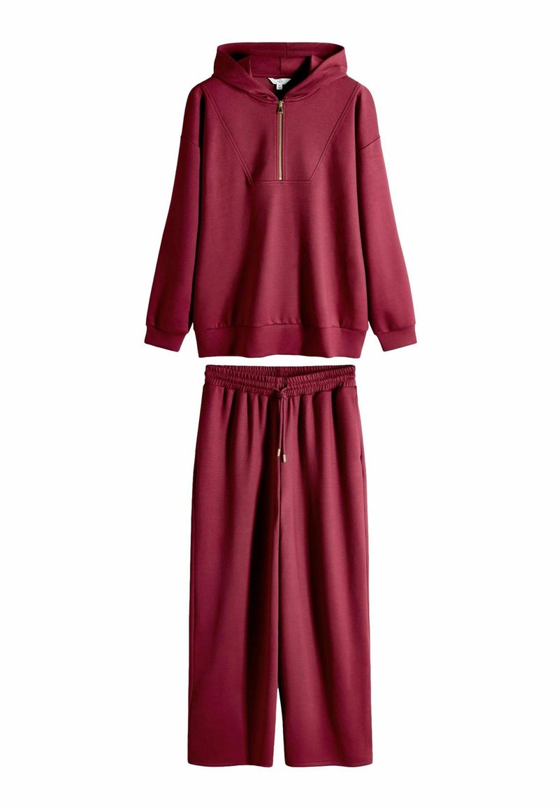 Bordo spalvos gobtuvu megztinis su pusiau užtrauktuku, derinamas su plačiomis tampriomis kelnėmis. Pagamintas iš minkštos, tekstūruotos medžiagos su elastiniu juosmeniu.