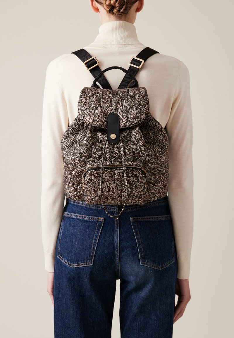 Textured black and beige backpack with drawstring closure and front zip pocket. Features black straps and a rounded flap.