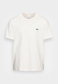 Krémové tričko s krátkým rukávem vyrobené z měkkého materiálu, s melírovaným vzorem, kulatým výstřihem a zeleným logem Lacoste na prsou.