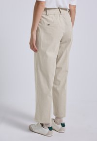 Beige corduroy broek met een elastische tailleband, voorzien van een ontspannen pasvorm, verticale ribbels en twee achterzakken.