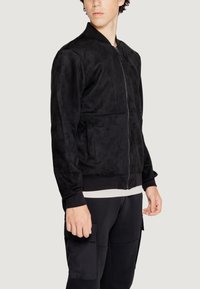 Giacca bomber nera con una morbida texture simile alla suede, dotata di una zip frontale, polsini a coste e due tasche laterali.