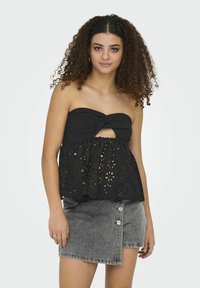 Top nero senza spalline con un dettaglio attorcigliato sul busto e un fondo in pizzo ad occhiello svasato, abbinato a una gonna in denim grigia con dettagli di bottoni.