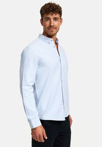 Maglietta a maniche lunghe azzurro chiaro con colletto button-down, dotata di bottoni marroni e orlo dritto. Tessuto liscio con una consistenza morbida.