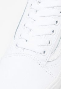 Baskets en toile blanche avec lacets et œillets blancs. Design minimaliste, comprenant des détails de couture et un panneau latéral texturé.