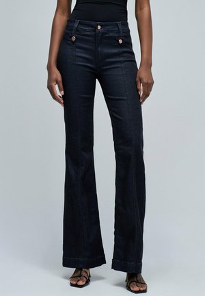 Vaqueros de tiro alto en denim negro, acampanados, con bolsillos frontales decorativos, doble cierre de botón y un acabado liso, ligeramente texturizado.