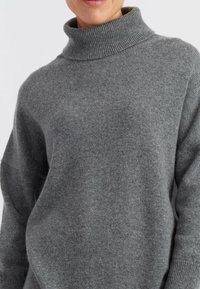 Maglione grigio con colletto alto a costine. Realizzato in materiale morbido, presenta una vestibilità comoda e spalle scese per un maggiore comfort.