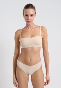 Beżowy dwuczęściowy strój kąpielowy składający się z topu bez ramiączek o gładkim wykończeniu oraz dopasowanych, niskich majtek. Prosty design bez wzorów czy akcentów.