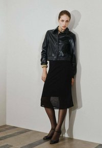 Veste en cuir noir courte avec fermeture à bouton et ourlet côtelé, associée à une jupe noire mi-longue avec un panneau inférieur en voile.