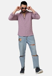 Camicia texture viola chiaro con chiusura a bottoni, abbinata a jeans azzurri strappati e sneakers nere.