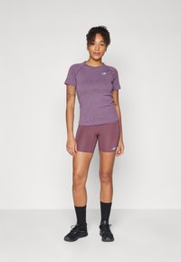 T-shirt de sport violet avec des manches courtes et un short assorti, arborant un logo. Des chaussettes noires et des chaussures complètent le look sportif.