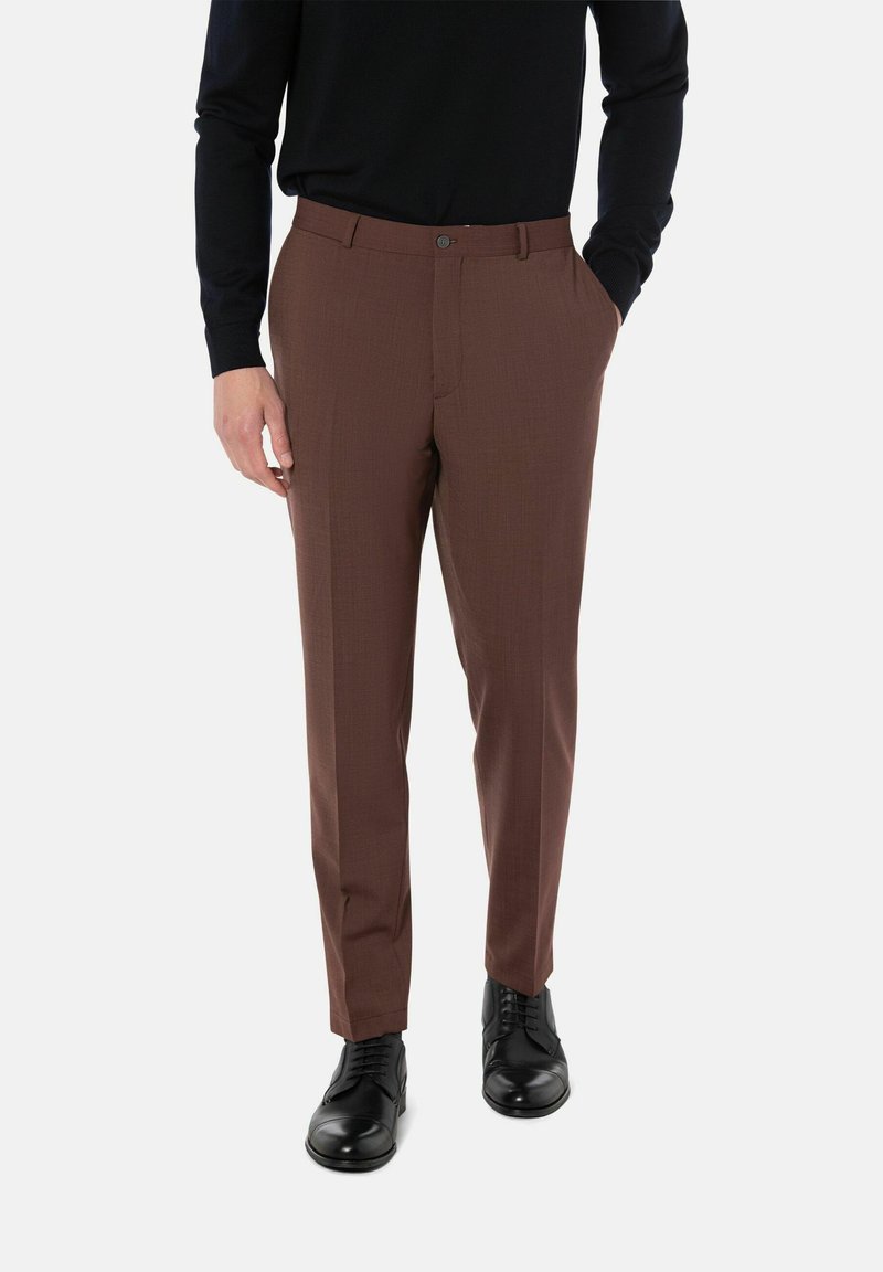 Bruine op maat gemaakte broeken met een strakke pasvorm, gestructureerde stof, zijzakken en een knoopsluiting, gecombineerd met zwarte nette schoenen.