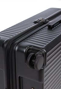 Valigia rigida nera con texture rigata, chiusura a zip e ruote doppie. Caratterizzata da una maniglia robusta e una finitura lucida e durevole.