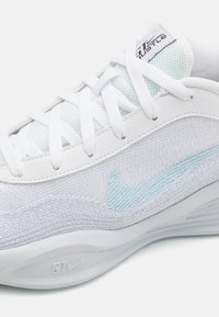 Hvid atletiksko med en struktureret overdel, lyseblå Nike swoosh og hvide snørebånd. Glat mellemsål med diskret branding.