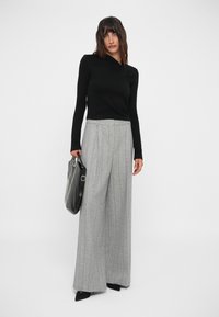 Musthave pikkade varrukatega must blouse ja hallid laiad triibulised püksid. Mudel hoiab käes musta käekotti. Viimistletud terava musta kingapaariga.