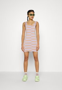 Strap dress in lilac and beige stripes, ribbed texture. Features a fitted shape and buttons down the front. Paired with green clogs.