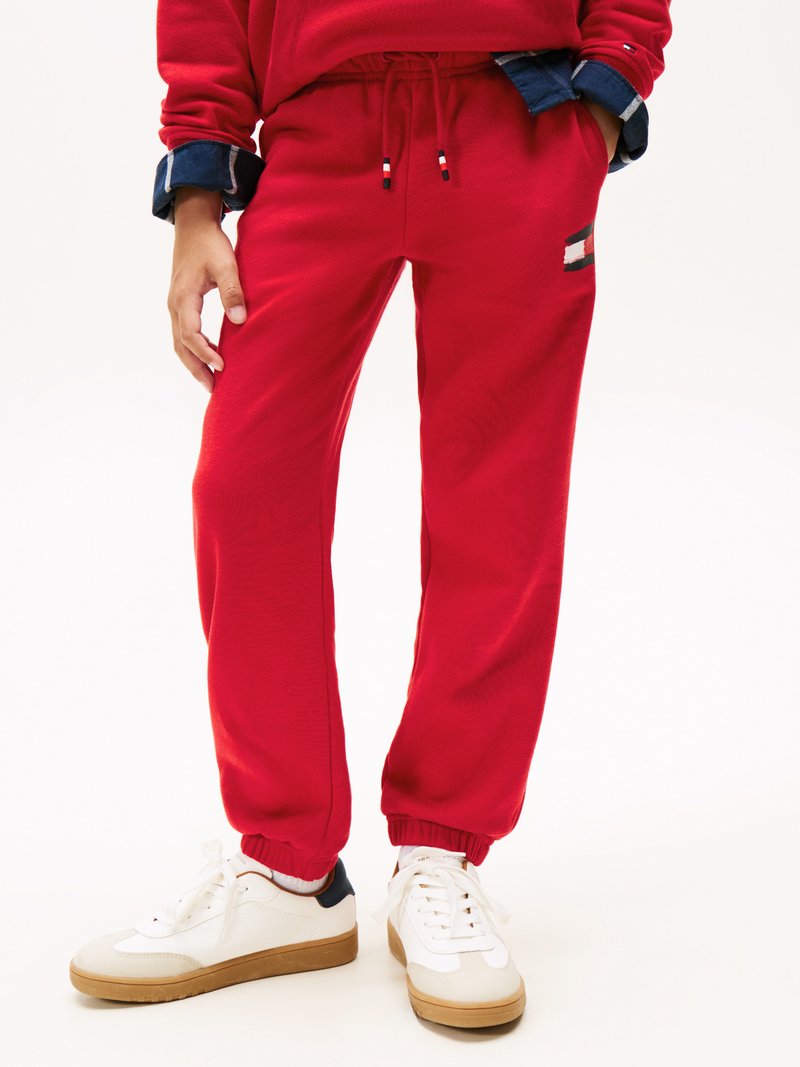 Rode joggingbroek met elastische boorden en een trekkoord in de taille, voorzien van een klein logo-opdruk aan de zijkant. Gecombineerd met witte sneakers.