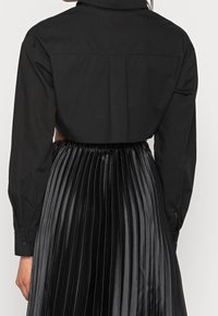 Black cropped shirt made of smooth fabric with long sleeves, paired with a pleated black skirt featuring a glossy texture.