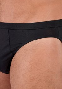 Bóxer de algodón negro con una textura suave, que presenta una cinturilla blanda y costuras mínimas. La vista lateral muestra un ajuste ceñido y sin patrones.