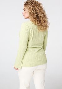 Lange mouwen top in lichtgroen, met een gestructureerd, golvend patroon. Gecoate, elastische stof en een aansluitend ontwerp passen mooi bij crèmekleurige broeken.