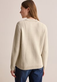 Lichtbeige gebreide trui met textuur, ronde halslijn, ribgebreide manchetten en zoom. Draag de trui met donkerblauwe denim, wat een casual pasvorm laat zien.