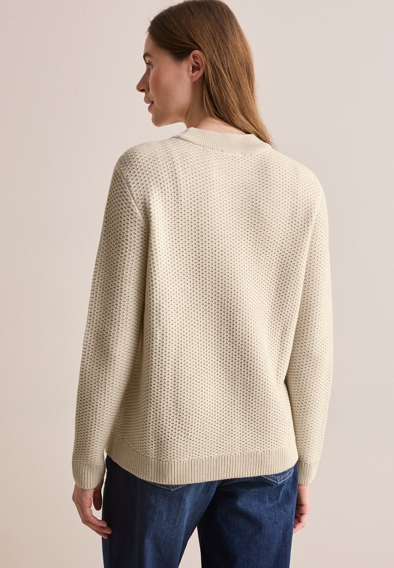 Lichtbeige gebreide trui met textuur, ronde halslijn, ribgebreide manchetten en zoom. Draag de trui met donkerblauwe denim, wat een casual pasvorm laat zien.