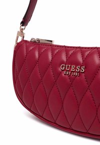 Borsa a tracolla in finta pelle rossa trapuntata con forma curva, hardware dorato e logo impresso. Dotata di una tracolla rimovibile per una maggiore versatilità.