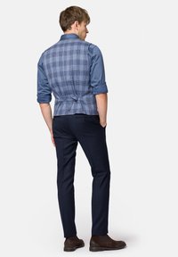 Niebieska kamizelka w kratę z tylnym wiązaniem, w połączeniu z ciemnymi spodniami. Kamizelka ma kontrastującą niebieską koszulę i brązowe botki za kostkę.