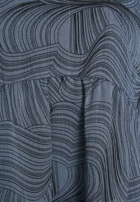 Tecido cinza escuro com padrões pretos ondulados; textura plissada perto da bainha. Material leve com um acabamento suave.