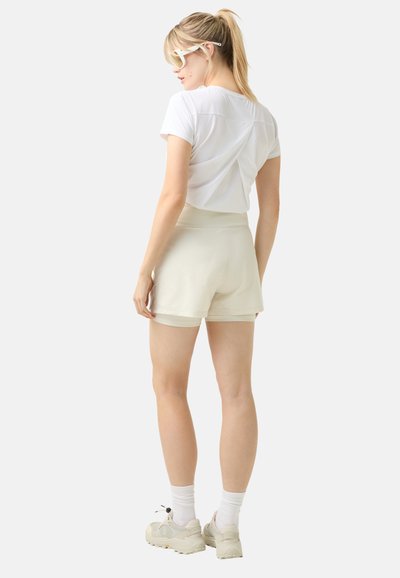 Witte cropped t-shirt met een gedraaide achterkant, gecombineerd met lichtbeige shorts. Beide kledingstukken hebben een gladde textuur. Casual schoenen zijn inbegrepen.