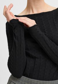 Top lung cu mâneci lungi, negru, texturat, cu decolteu off-shoulder. Prezintă modele ribbed și manșete desfăcute, asortat cu o fustă în carouri.