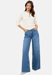 White and colorful striped knit cardigan with round neck and buttons, paired with loose blue denim wide-leg jeans. Silver shoes complete the look.