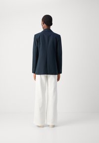 Námořnický blazer se strukturovaným designem a přiléhavým střihem, spárovaný s bílými širokými kalhotami. Hladká látka a minimalistické akcenty.